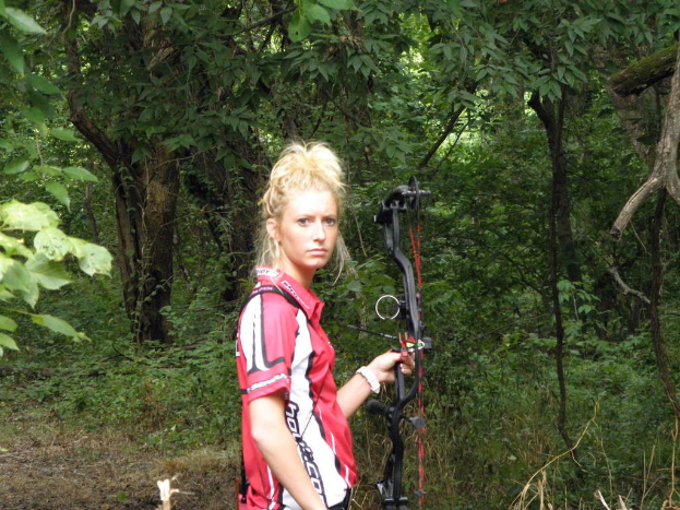 Eine Frau hält einen Bogen mit einigen Bäumen im Hintergrund.