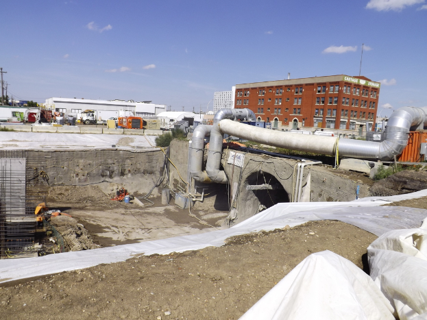 Eine Szene mit Gebäuden, einem Zaun, Fahrzeugen, aktuellen Umfragen, einem Rohr und dem Himmel darüber.