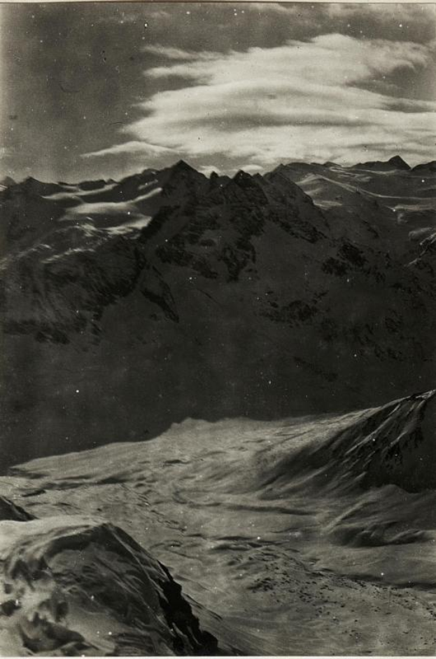 Ein Schwarz-Weiß-Foto einer schneebedeckten Gebirgskette mit einem bewölkten Himmel und einem Text am unteren Rand, der 'Gustav Klimt - The Alps' lautet.