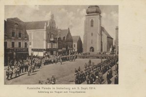 Ein Schwarz-Weiß-Foto einer Parade in Insterburg am 5. September 1914 mit vielen Menschen, Gebäuden im Hintergrund und Text am unteren Rand des Bildes.
