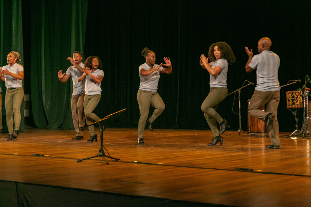 Ein Schwarz-Weiß-Foto eines Paares, das auf einer Bühne tanzt, mit ein paar Menschen auf einer Treppe im Hintergrund und einem Pfahl im Vordergrund.