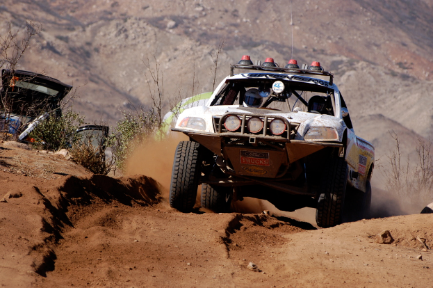 Ein weißes Auto bewegt sich in der Mitte des Bildes, mit grünen Pflanzen auf der linken Seite.