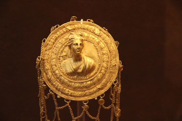 Goldene Medaille mit einer Frauengestalt, die detailliert verziert ist, vor einem dunklen Hintergrund.