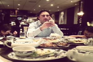 Ein Mann sitzt an einem Tisch mit einem Kessel, Teller, Löffel und Lebensmitteln.