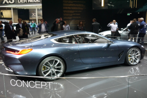 Ein BMW 8er-Konzeptfahrzeug mit glänzendem Schwarz und Chromakzenten wird auf der IAA in Frankfurt präsentiert, umgeben von Menschen, die Fotos machen, mit einem hell beleuchteten Hintergrund und einem Textschild im Bild.