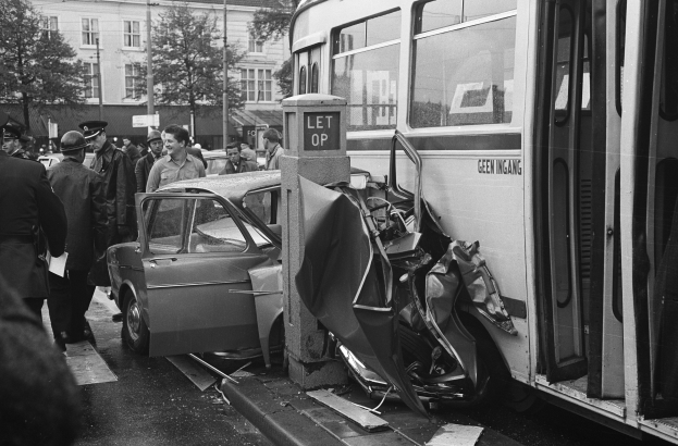 Schwarz-weißes Bild eines Bus, der auf der Seite der Straße in ein Auto gekracht ist, mit Menschen und Bäumen im Hintergrund.
