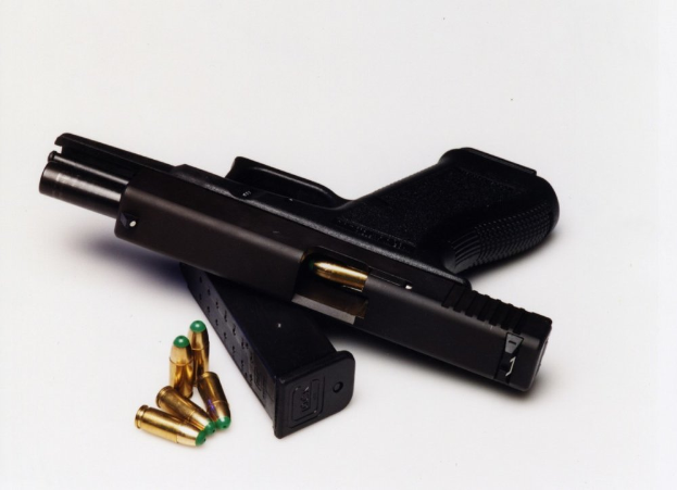 Eine schwarze Handfeuerwaffe mit einem Magazin und Patronen auf einer weißen Oberfläche.