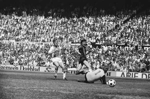 Schwarzes und wei├čes Foto von M├Ąnnern, die auf einem Feld Fussball spielen, mit Zuschauern im Hintergrund und einer Bundesliga 1978-79 Ajax 1-1 Hannover 96 Fahne.