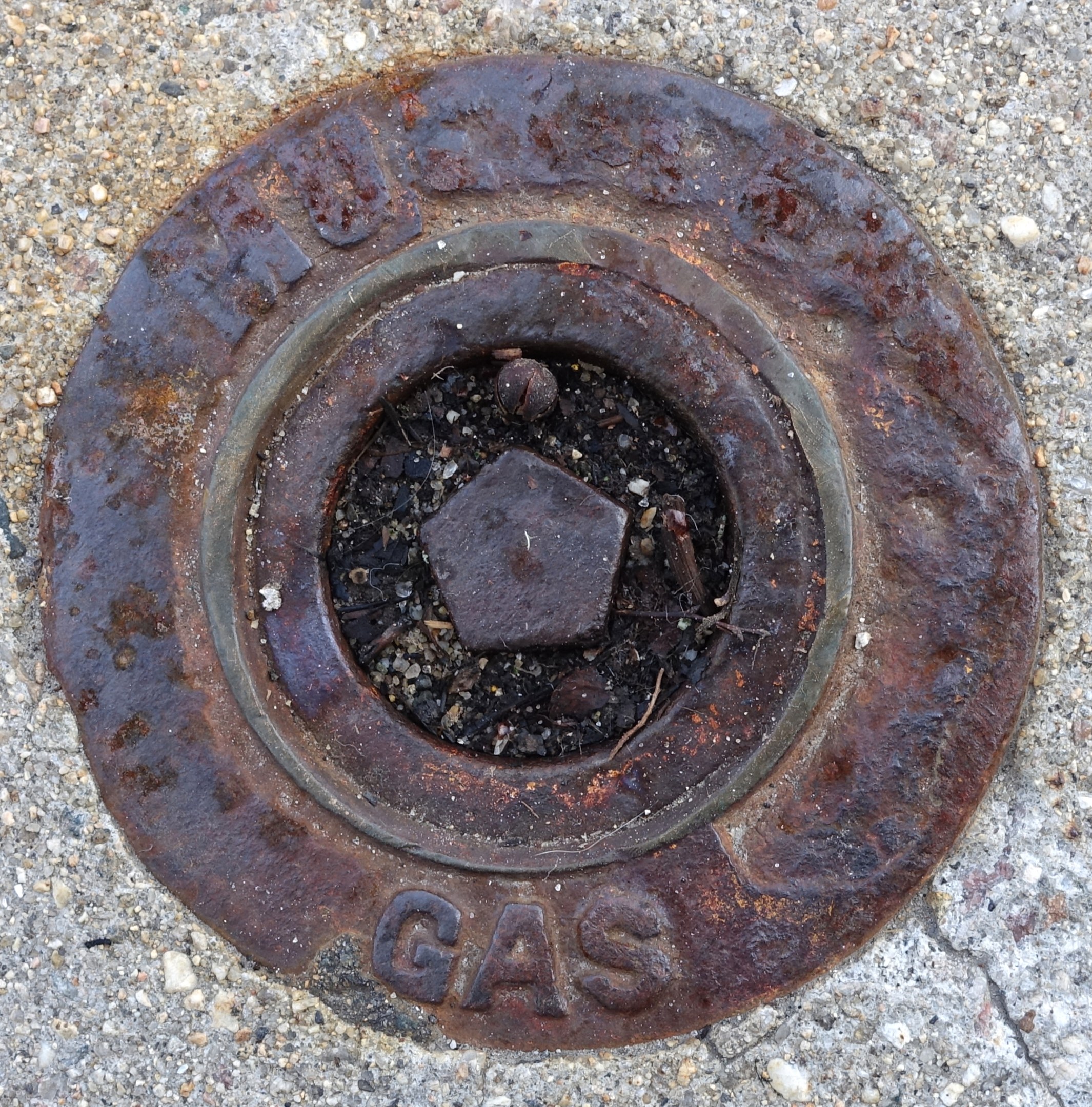 Ein verrosteter Metall-Schachtobdeckel auf dem Boden mit dem Wort 'Gas' darauf geprägt.