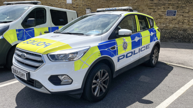 Zwei Polizeiwagen nebeneinander auf einem Parkplatz geparkt, mit einer Wandtafel im Hintergrund.