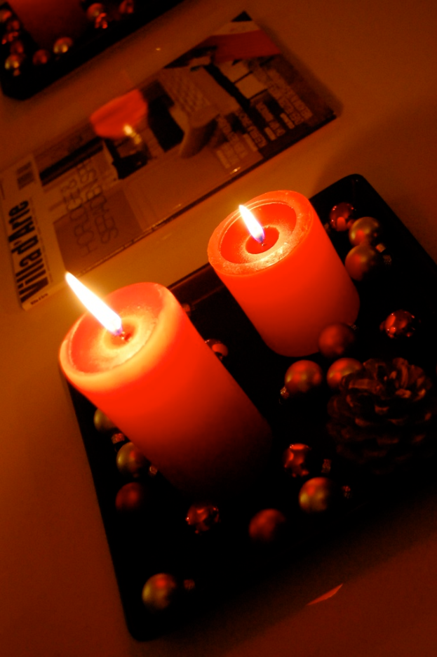 Zwei rote Kerzen in einer schwarzen Schale auf einem Tisch, mit einem Buch daneben.