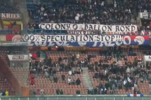 Ein Stadion mit einer großen Menschenmenge, Schildern und Stühlen, mit einem Zaun unten und einer Treppe links.