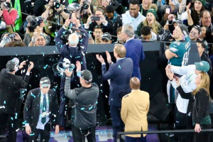 Philadelphia Eagles-Spieler feiern mit dem Vince Lombardi Trophy nach dem Gewinn des Super Bowls, einige halten den Pokal und andere werfen Konfetti, mit einem Geländer und Fotografen im Hintergrund.