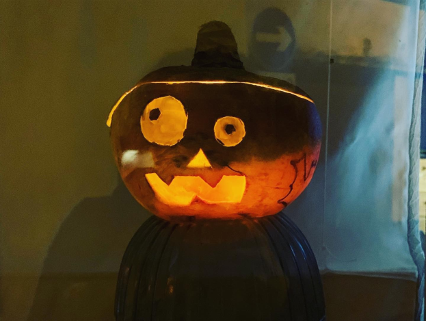 Eine geschnitzte Kürbis mit einem Gesicht, von innen beleuchtet, steht auf einem Tisch mit einer Wand und Vorhang im Hintergrund, schafft eine gruselige Halloween-Atmosphäre.