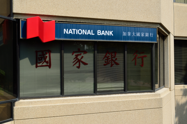 Ein Gebäude mit Glasfenstern und einem Schild mit der Aufschrift "National Bank" auf Englisch und Chinesisch, mit einer Pflanze auf der linken Seite, die eine neue Filiale in Hong Kong ankündigt.