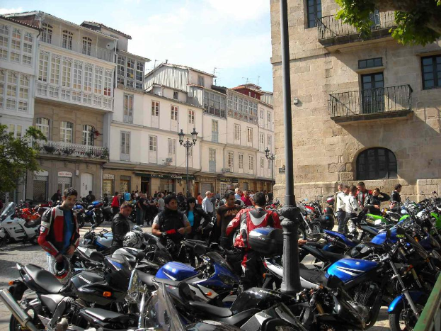 Ein cremefarbenes Gebäude mit zahlreichen Fenstern, das an ein Backsteingebäude mit einer Metallbalustrade angrenzt, mit mehreren parkenden Fahrrädern und Menschen, die vor dem Gebäude sprechen.