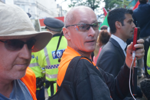 Eine Gruppe von Menschen, die mit einer Person mit einer Mütze auf der linken Seite und einem Polizisten im Hintergrund stehen.