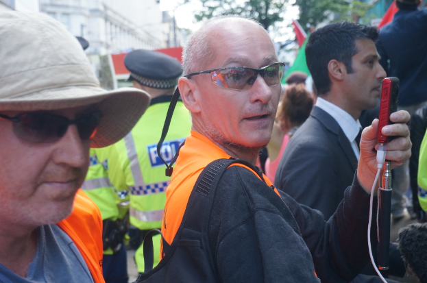 Eine Gruppe von Menschen, die mit einer Person mit einer Mütze auf der linken Seite und einem Polizisten im Hintergrund stehen.