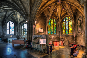 Ein Raum mit Bänken, Tischen, einer Tafel, Fenstern, einer Wand, Kerzen und einem Kamin in der Mitte, bearbeitet.