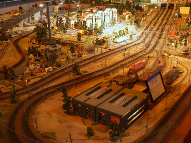 Eine detaillierte Modellbahnausstellung in einem Museum, die Miniaturgebäude, Bäume, Eisenbahnschienen, Fahrzeuge, Pfosten, Lichter und Schilder zeigt, die eine belebte Stadtlandschaft nachahmen.