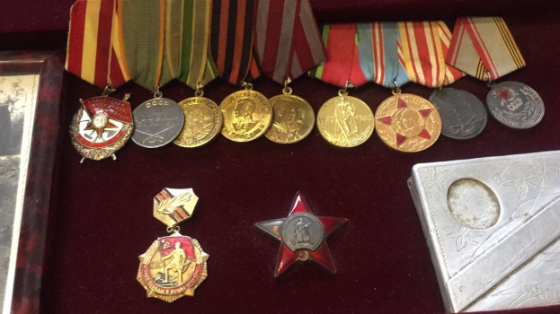 Eine hölzerne Kiste mit verschiedenen Medaillen, darunter ein roter Stern als Symbol der Sowjetunion, ordentlich mit einem Objekt auf der rechten Seite angeordnet.