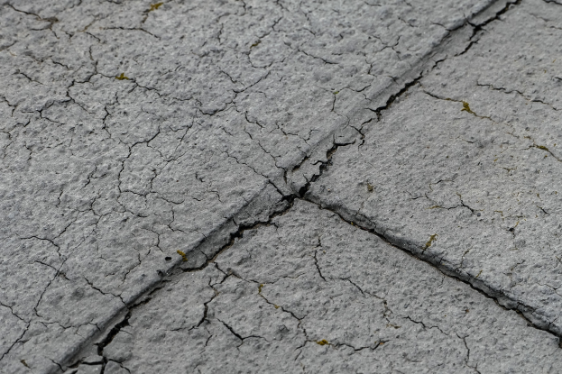 Nahaufnahme einer gebrochenen, verwitterten Straßenoberfläche mit tiefen, breiten Rissen.