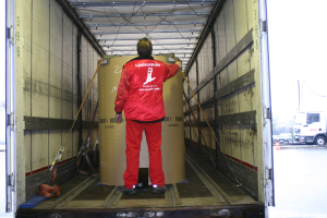 Eine Person hält eine Trommel in einem Lkw, mit mehreren Fahrzeugen auf der Straße außerhalb.