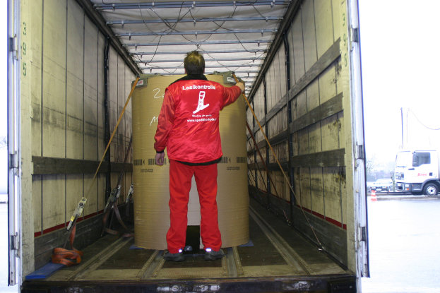 Eine Person hält eine Trommel in einem Lkw, mit mehreren Fahrzeugen auf der Straße außerhalb.