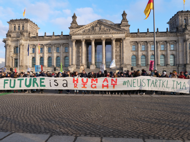 Eine Gruppe von Menschen steht vor dem Reichstaggebäude in Berlin, Deutschland, und hält ein Banner mit der Aufschrift "Zukunft ist ein Mensch"