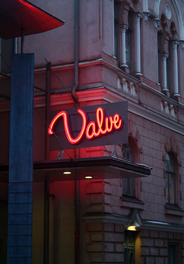 Ein Gebäude mit Fenstern, einer Tür, einem Pfahl und einer leuchtenden Neon-Schriftzug 'Ventil', die eine warme und einladende Atmosphäre schafft.