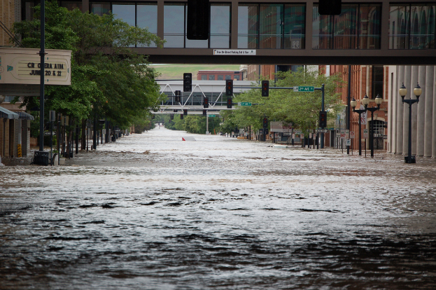 Eine überflutete Stadtstraße mit Wasser auf der Straße, Polen, Laternen, Schildern, Verkehrsampeln, Bäumen, Gebäuden und einer Brücke im Hintergrund.