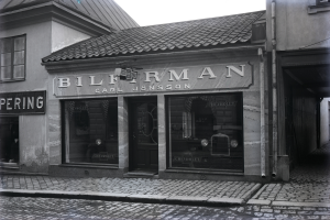 Ein Schwarz-Weiß-Foto eines Gebäudes mit einer "Bilferman"-Aufschrift, Fenstern, einer Tür und Tafeln mit Text, mit einer Straße unten.