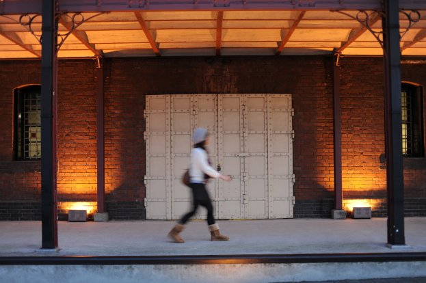 Eine Frau geht durch einen Korridor mit einer Metalltür in einem Gebäude.