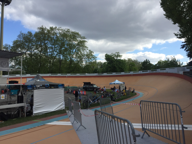 Gruppe von Radfahrern auf einer Schmutz BMX-Strecke bei den UCI BMX-Weltmeisterschaften 2018, mit Zelten, Fahrzeugen und Bäumen im Hintergrund.
