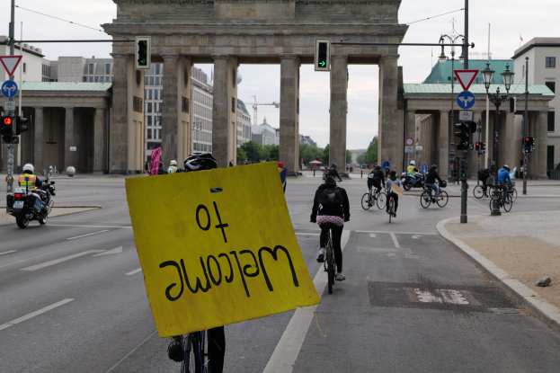 Eine Gruppe von Menschen auf Fahrrädern fährt eine Straße entlang vor dem Reichstagsgebäude in Berlin, Deutschland, mit Helmen und einer Person, die ein gelbes Schild hält.