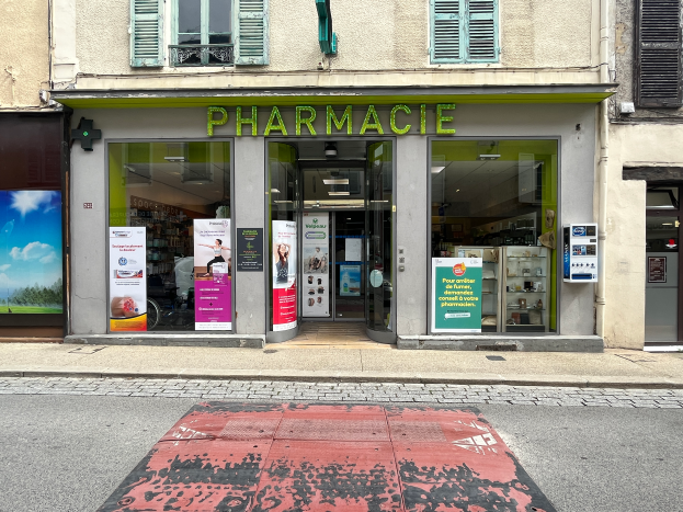 Eine Apotheke an einer Straßenecke mit Glaswänden und -türen, Plakate an den Wänden und eine Straße davor.