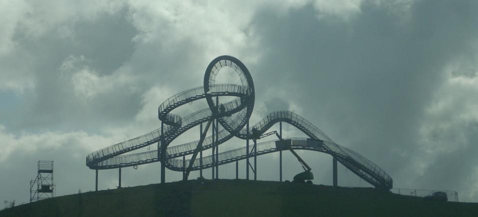 Eine Achterbahn auf dem Gipfel eines Hügels unter einem bewölkten Himmel, umgeben von Stützkonstruktionen.