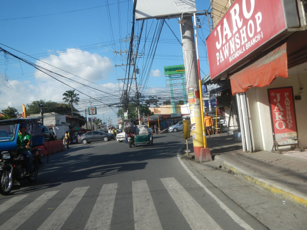 Eine belebte Stadtstraße mit Fahrzeugen, Fußgängern, Gebäuden und einem "Jaro Pfandleihhaus" auf der rechten Seite.