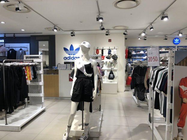 Innenansicht eines adidas-Ladens in Singapur mit Schaufensterpuppen, Kleiderständern, einem Textboard auf der rechten Seite und Deckenbeleuchtung.