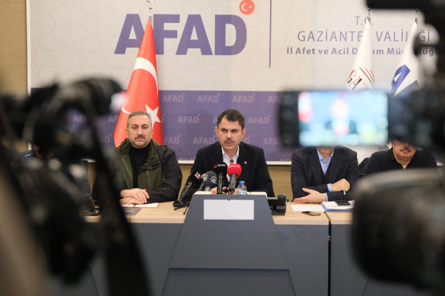 Eine Gruppe von Männern, die an einem Tisch mit Mikrofonen, Flaschen und Papieren sitzen, mit Flaggen und einer Tafel mit der Aufschrift "AFAADs Statement zur Situation in der Türkei" im Hintergrund und Kameras rechts daneben.