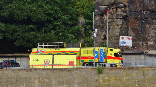 Ambulanz am Straßenrand neben einer Klippe mit Bäumen und einem Auto im Hintergrund.