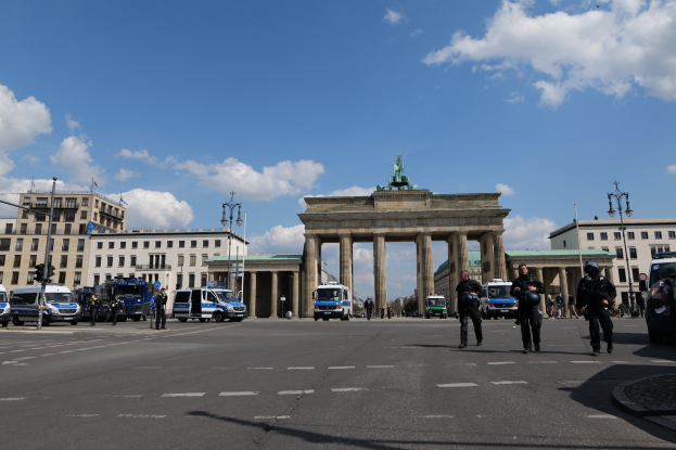 Polizisten vor dem Brandenburger Tor in Berlin, Deutschland, mit den Säulen und der Statue des Tors im Hintergrund, umgeben von Gebäuden und Fahrzeugen auf der Straße.