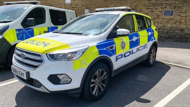 Zwei Polizeiautos nebeneinander auf einem Parkplatz geparkt, mit einer Wand und einer Tafel im Hintergrund.