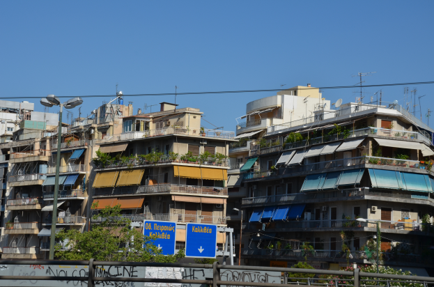 Eine Stadtansicht mit Gebäuden, Bäumen, Pfählen, Lampen, Drähten und Brettern im Vordergrund und einem klaren Himmel im Hintergrund, die Graffiti an der Seite eines Gebäudes zeigt.