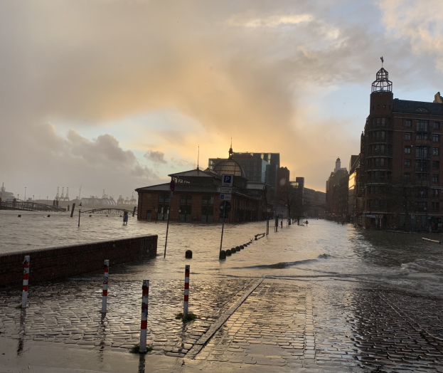 Überflutete Straße in Hamburg, Deutschland, mit Wasser, das die Straße, Pfosten, Schilder, Gebäude und eine Brücke bedeckt.