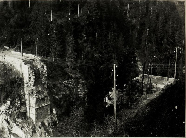 Ein Schwarz-Weiß-Foto einer Brücke über einen Fluss mit Bäumen, Pfählen und Felsen im Hintergrund, mit dem Text "Brückenbau der 1930er Jahre" unten.