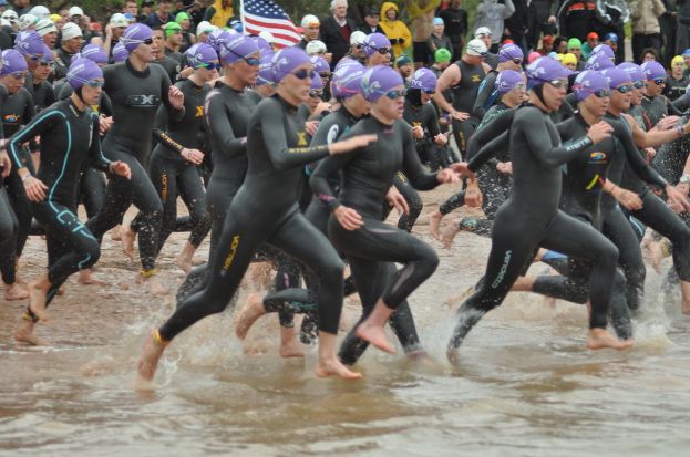 Menschen in Badeanzügen im Wasser laufen, mit anderen im Hintergrund und einer Flagge im Bild.